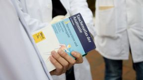 Eine Person in einem Arztkittel hält ein Medizinbuch in der Hand.