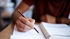 Studierender schreibt mit einem Bleistift in ein Prüfungsheft